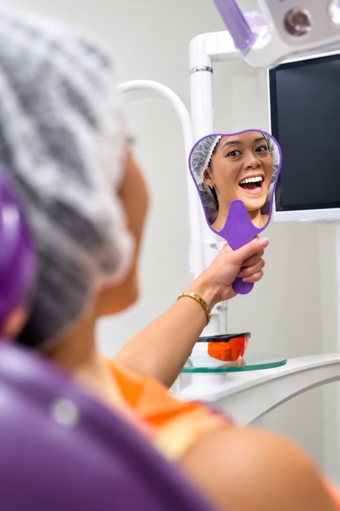 A patient smiling at her reflection after a visit to Home of Dental Aesthetics